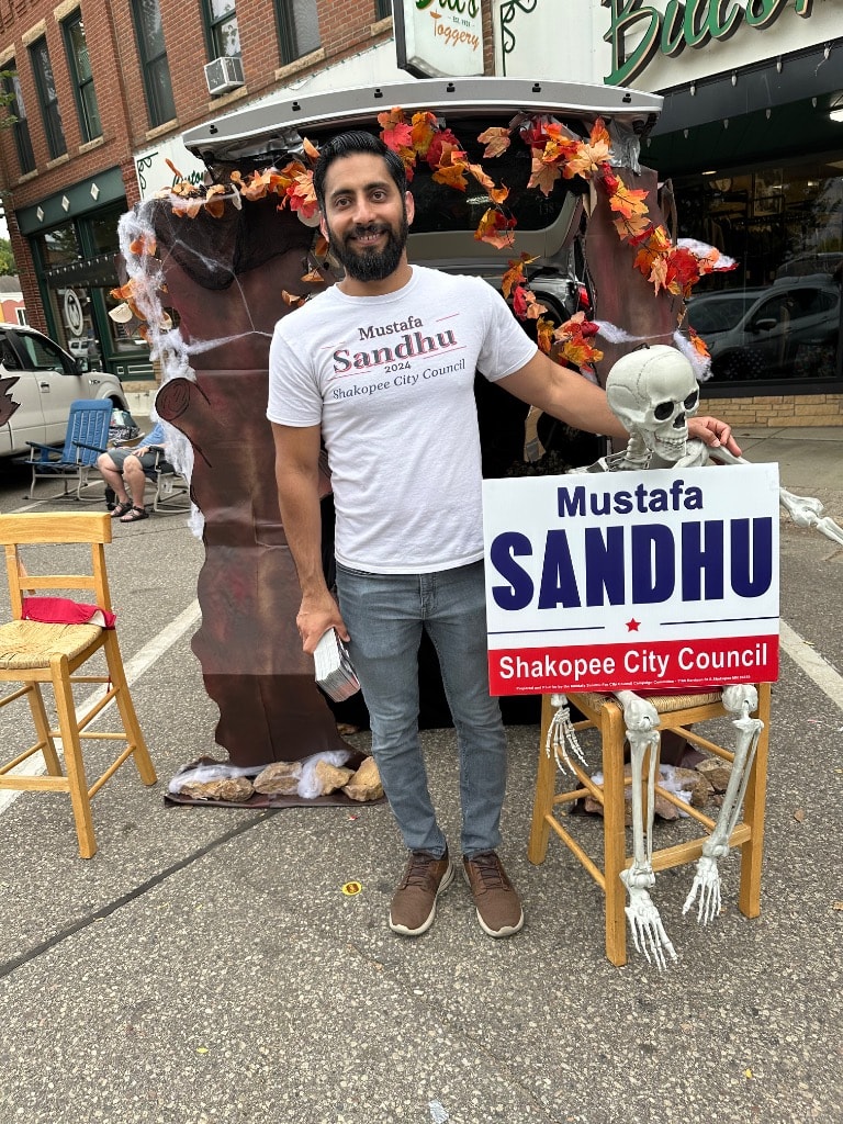 Mustafa Sandhu posing with his campaign sign at the decorated trunk-or-treat booth