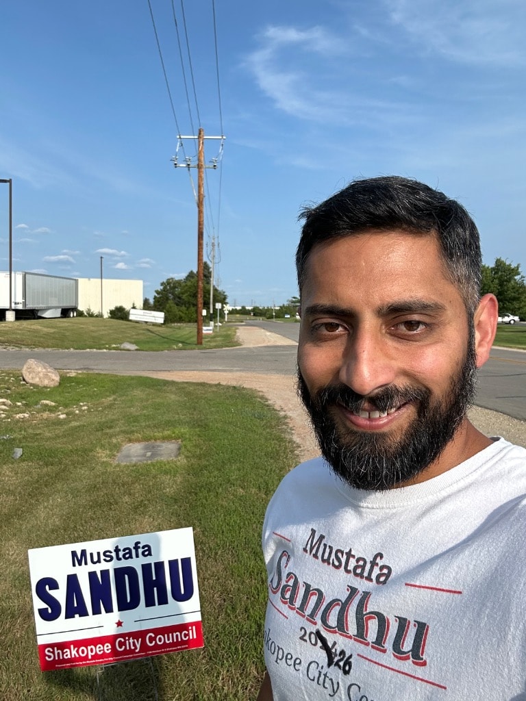 Man holding a Sandhu political campaign sign outdoors