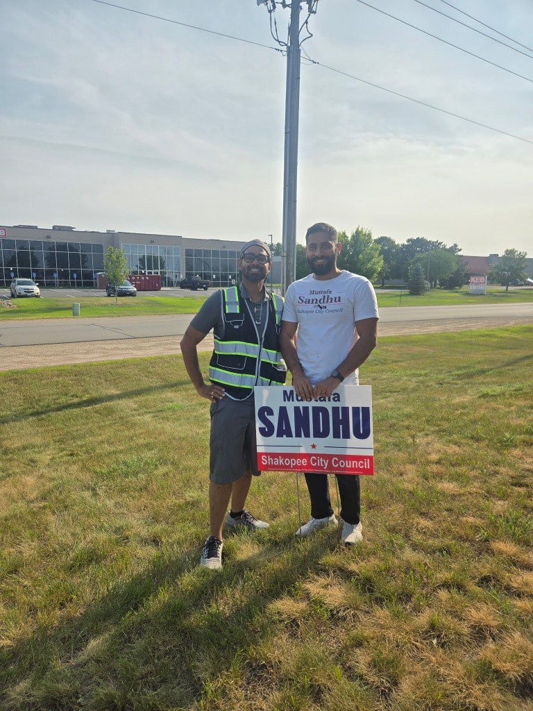 Two men holding a Sandhu campaign sign outdoors