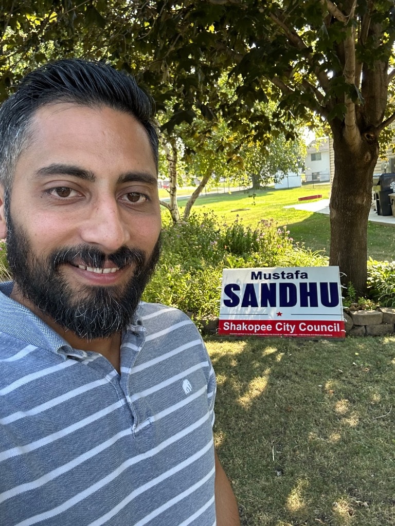 Man posing with a political campaign sign outdoors