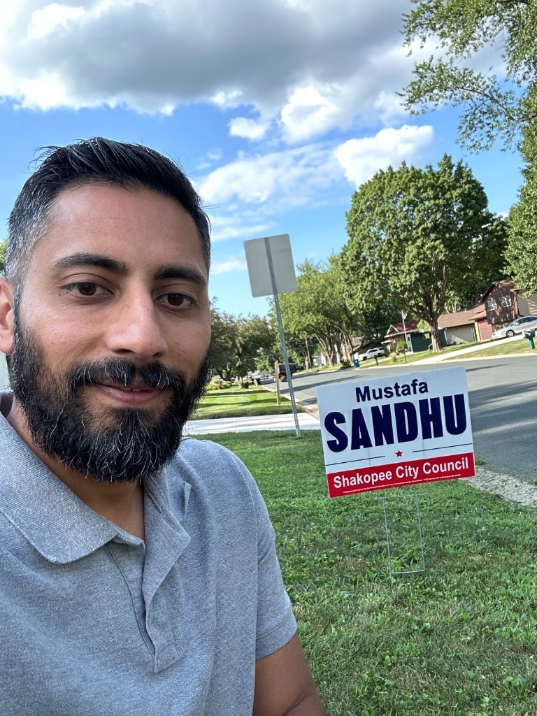 Mustafa Sandhu posing with a campaign yard sign