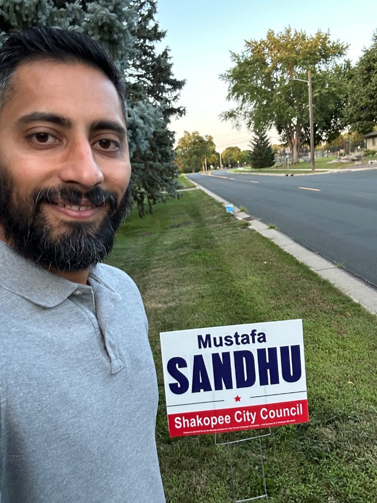 Mustafa Sandhu holding a campaign sign outdoors