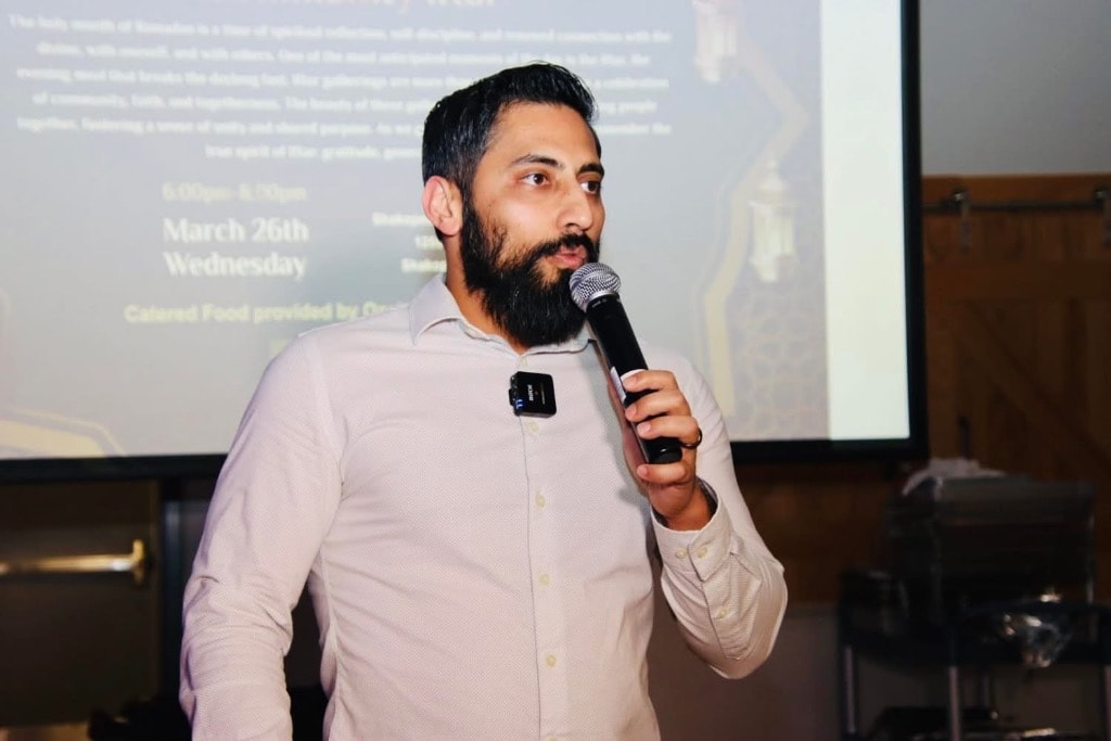 Mustafa Sandhu speaking into a microphone at a community Iftar event
