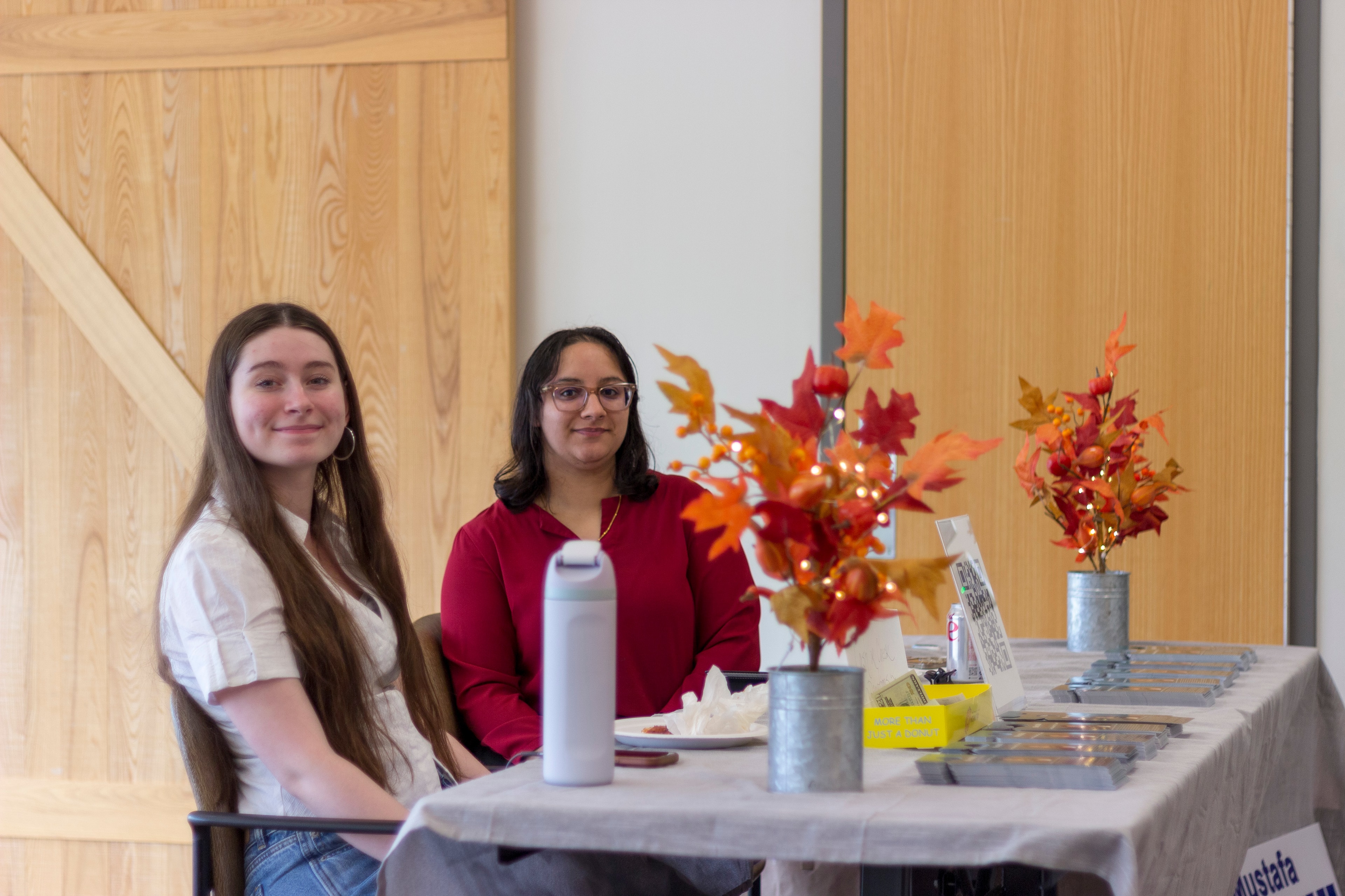 Two volunteers smiling at the autumn-decorated welcome table