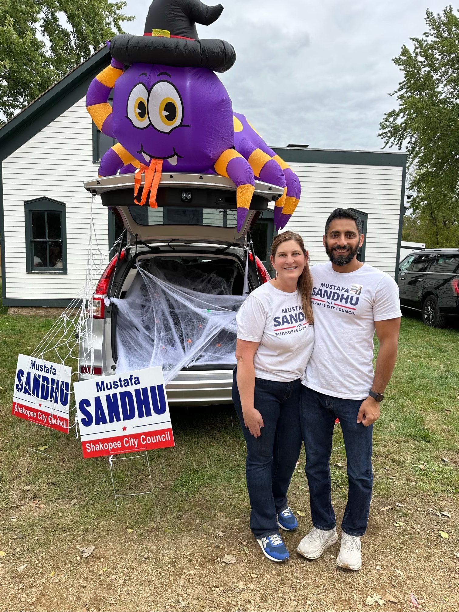 Mustafa Sandhu and his wife posing in front of their decorated trunk with inflatable spider