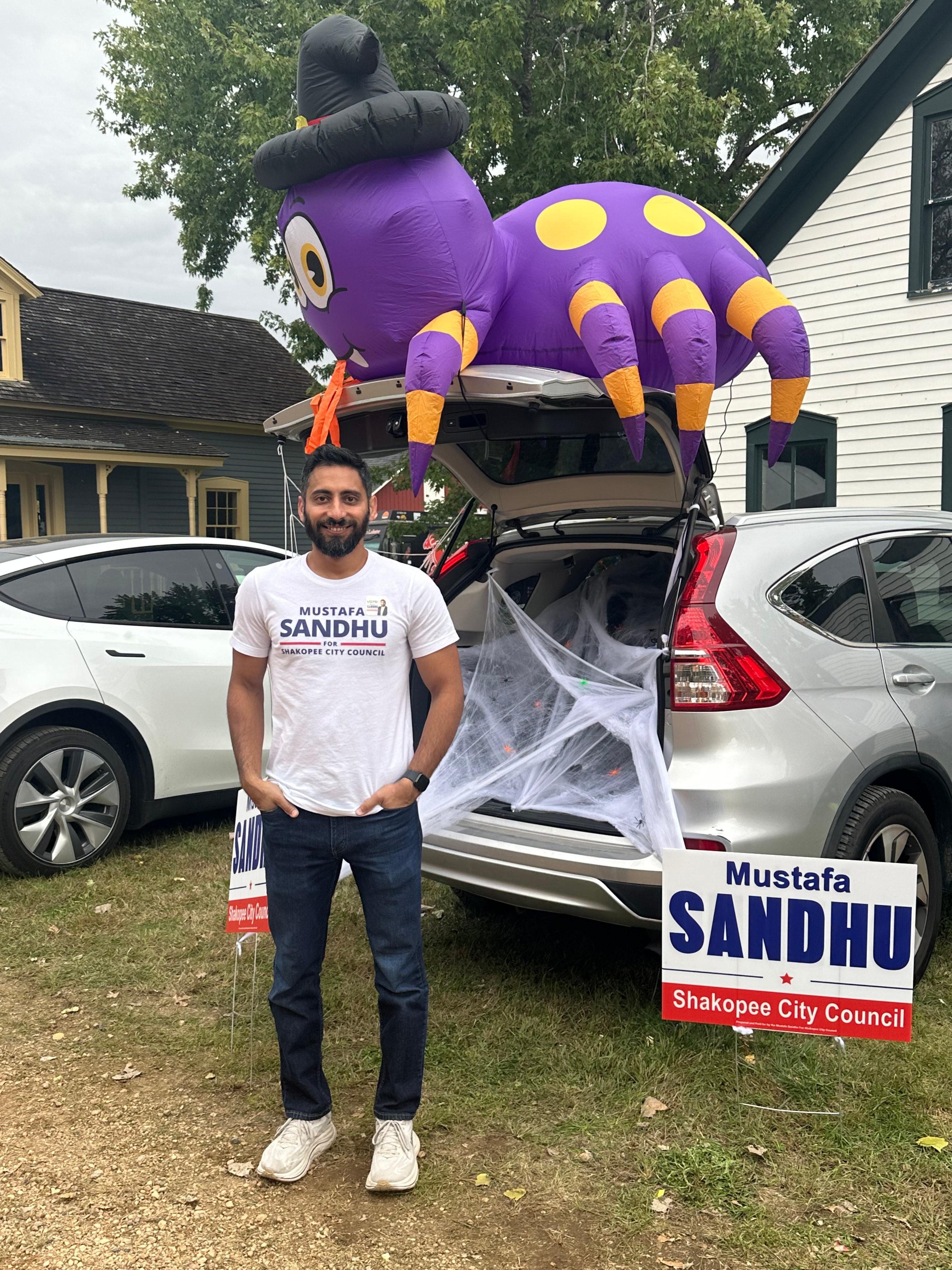 Mustafa Sandhu posing with inflatable spider decoration and campaign signs