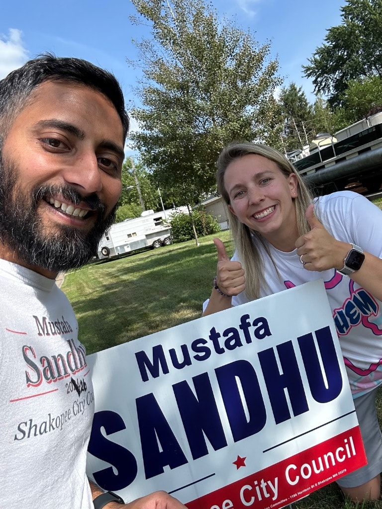 Couple holding a Sandhu campaign sign outdoors