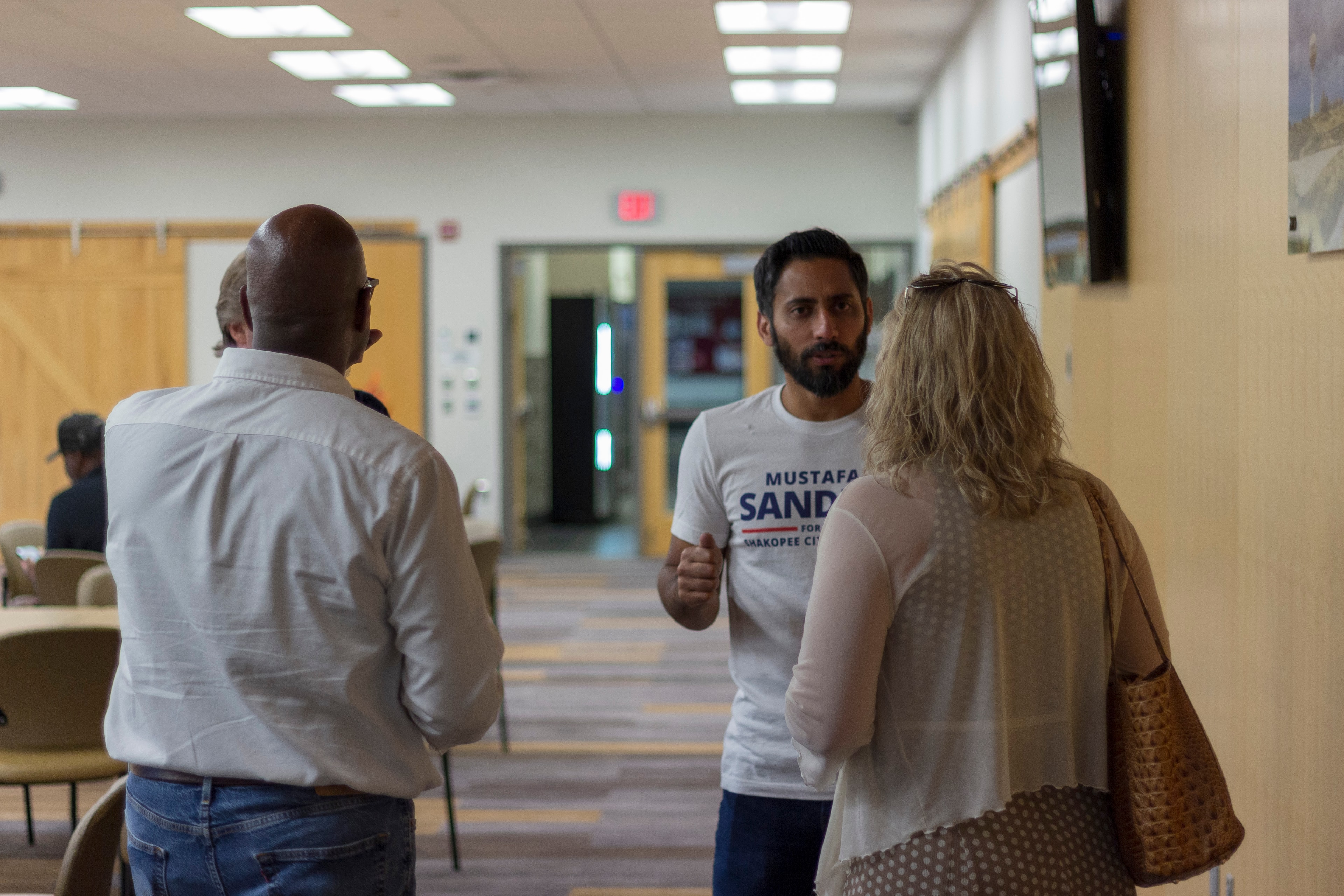Mustafa Sandhu in campaign shirt speaking with two attendees in hallway